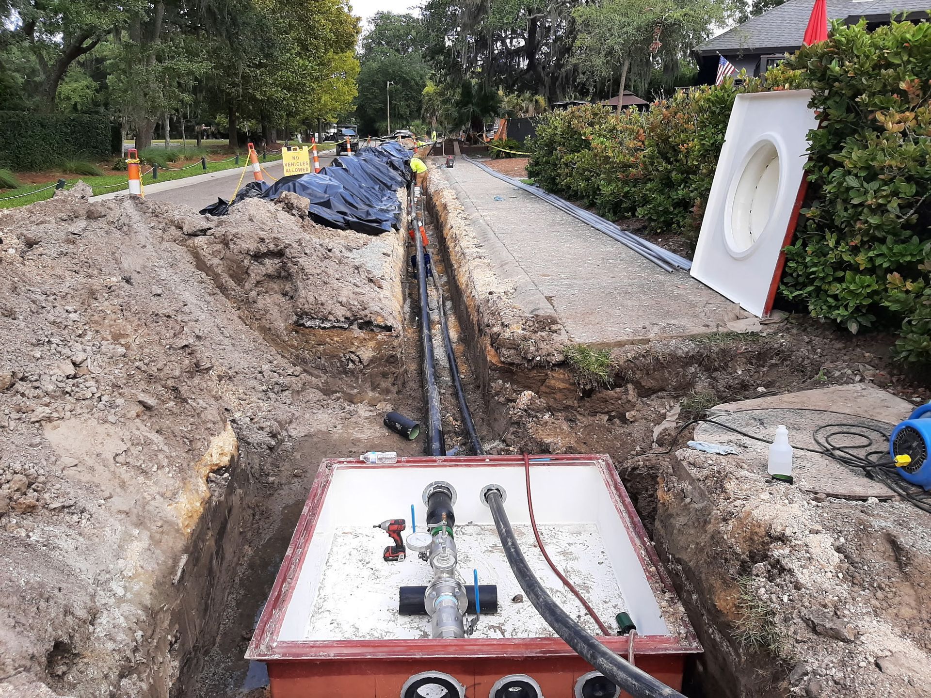 Trench dug alongside road with buried pipes, electrical box. Construction site.
