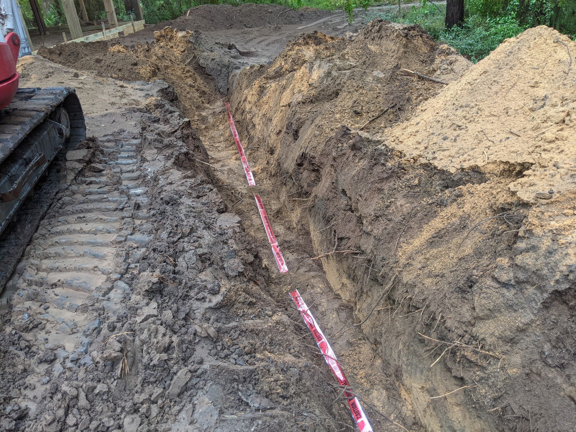 Trench dug in muddy ground with red and white striped utility line and an excavator.