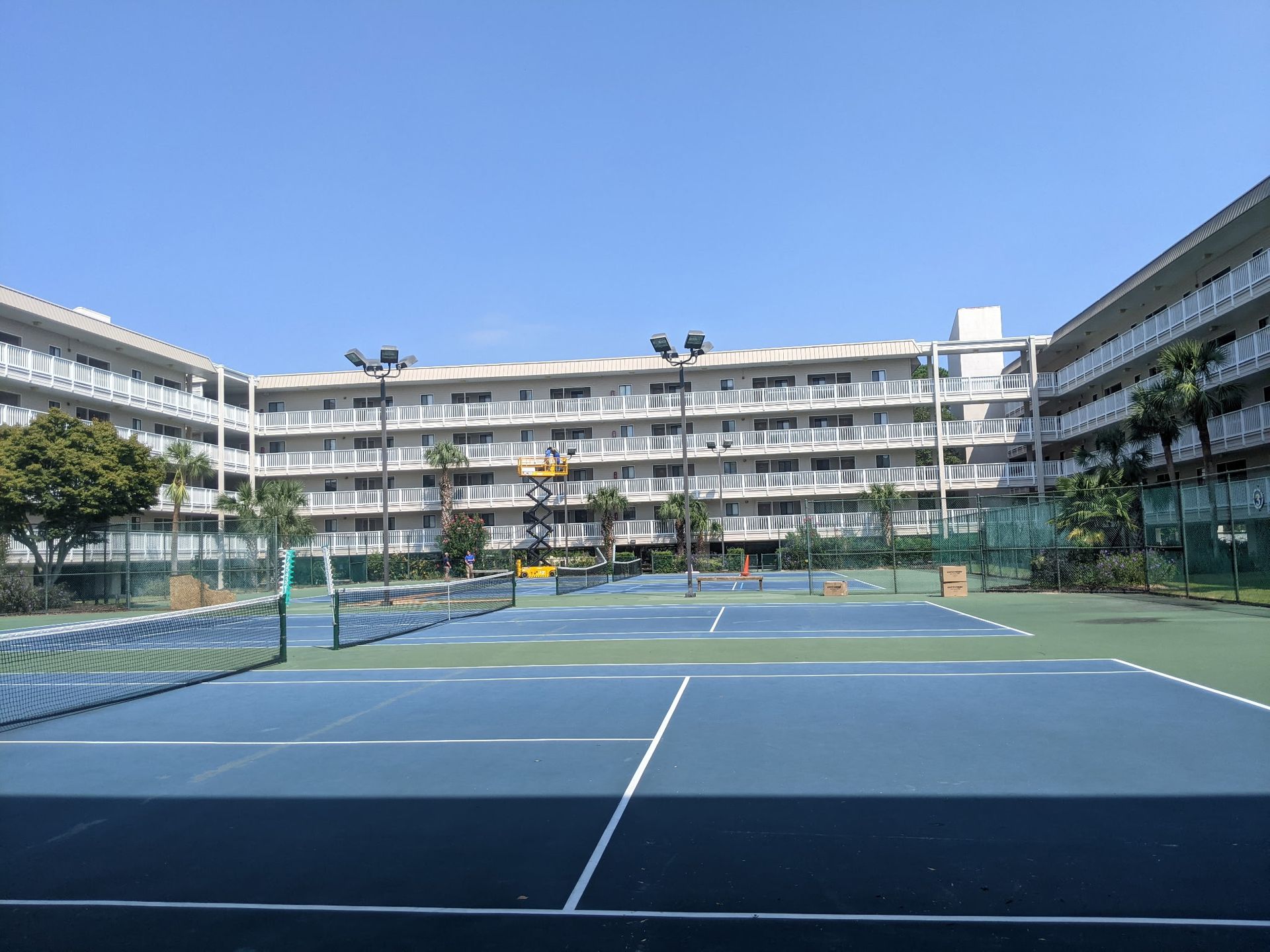 Tennis court in front of a multi-story building on a sunny day.