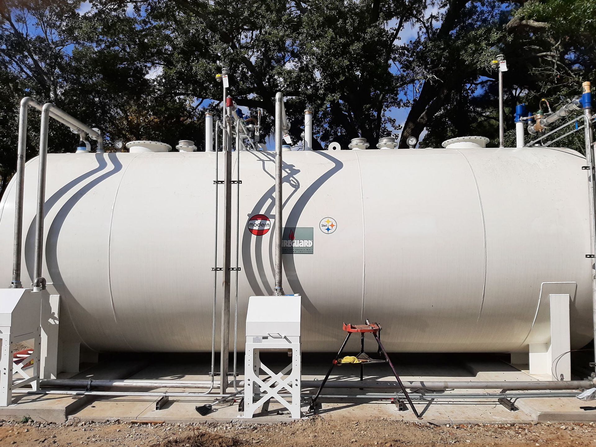 Large white industrial tank with piping, gauges, and a small step ladder outdoors.