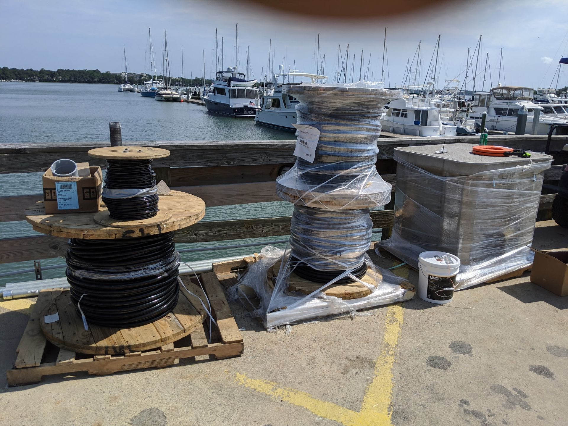 Spools of black cable on a dock near a marina. Some are on wooden pallets.