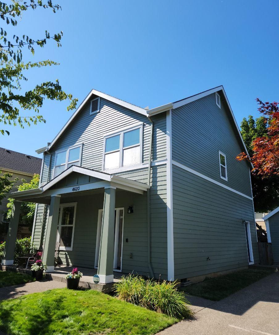 Gray two-story house with white trim, front porch, and green lawn under a blue sky