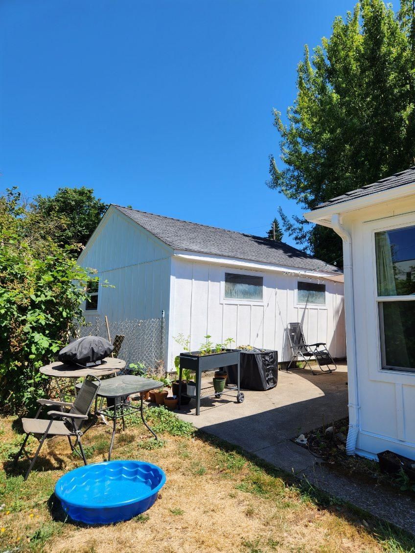 Sunlit backyard with white sheds, patio furniture, and a blue kiddie pool on dry grass.