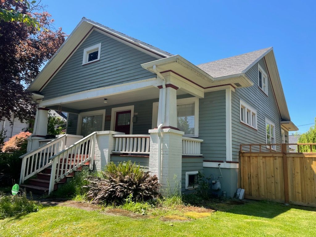 Gray house with white trim, front porch, steps, and a wooden fence in a sunny yard