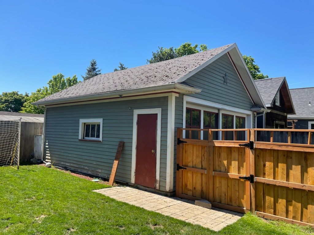 Small gray shed with red door beside a wooden fence in a sunny backyard