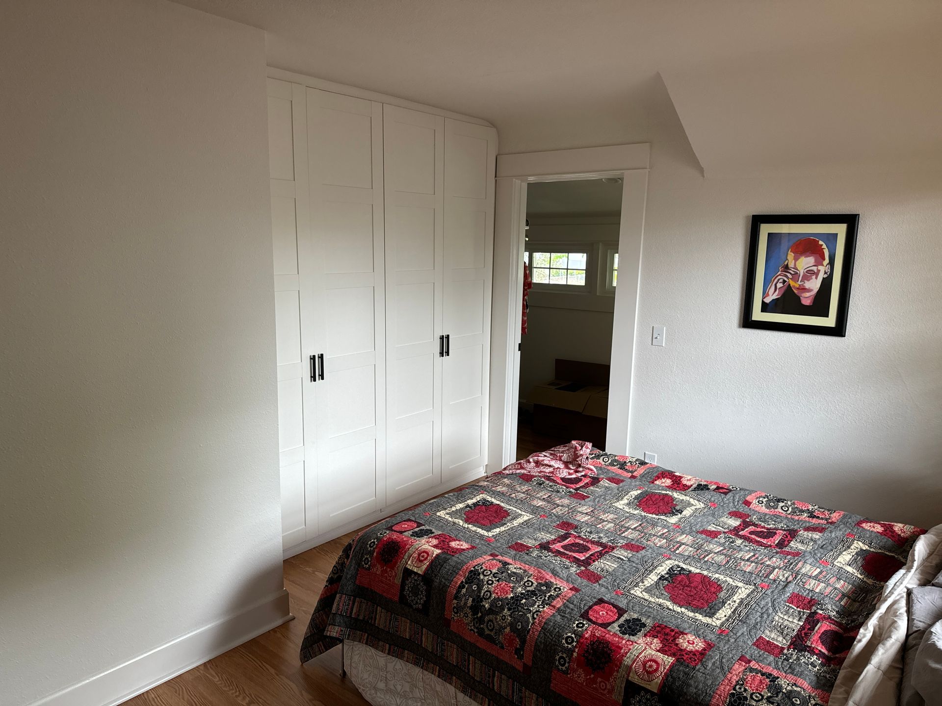 Small bedroom with a red patterned bedspread, white built-in cabinets, and a framed wall print.