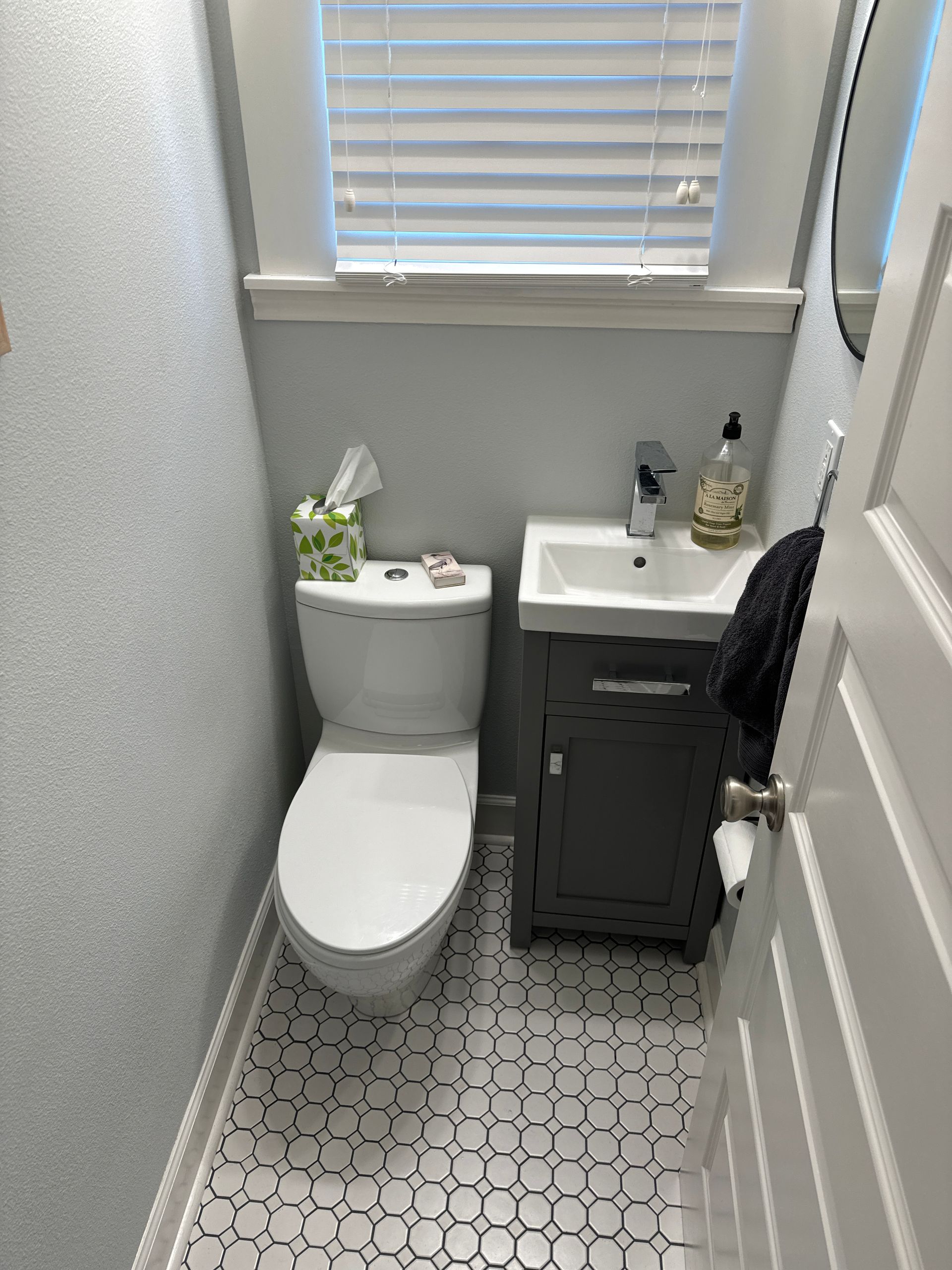 Small bathroom with toilet, sink cabinet, patterned floor, and window above the sink.