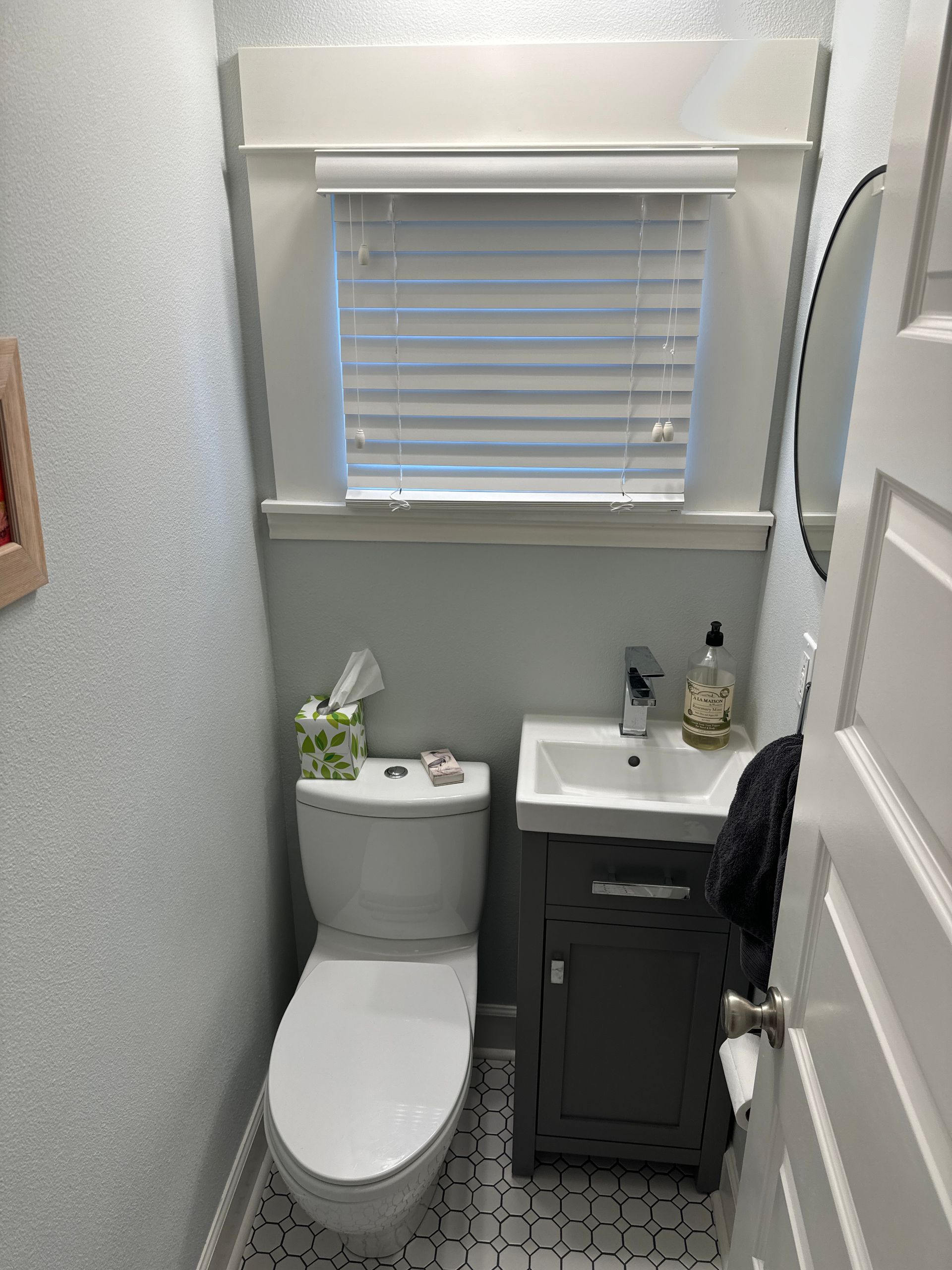 Small narrow bathroom with a toilet, sink cabinet, window blinds, and gray walls.