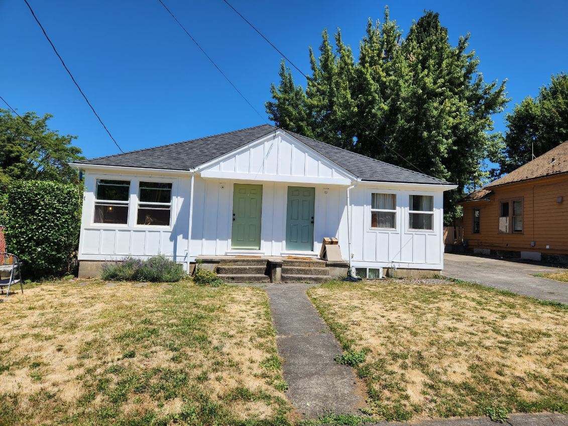 Small white bungalow with a front porch, walkway, and dry lawn under a blue sky