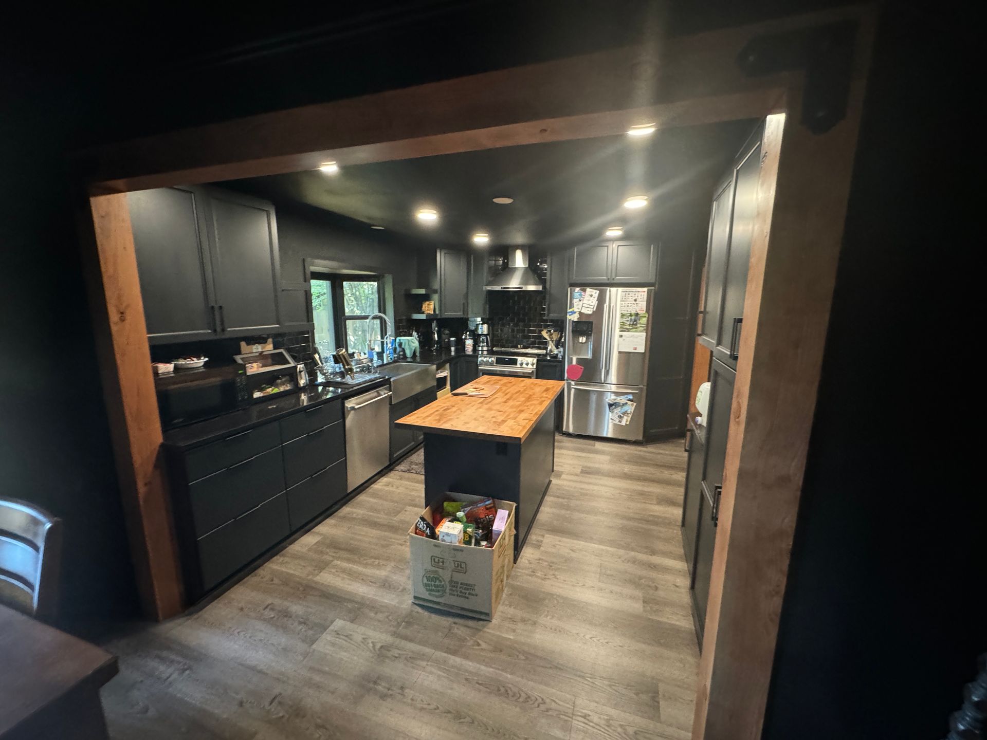 Modern kitchen with dark cabinets, wood island, and stainless steel refrigerator on wood-look flooring