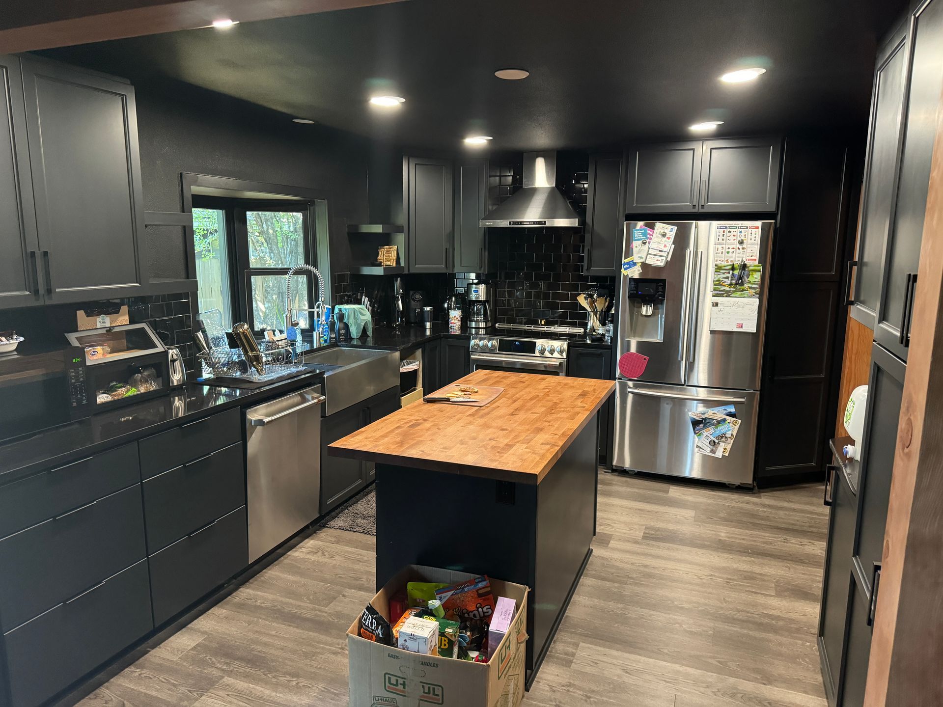 Modern black kitchen with wood island, stainless appliances, and large windows