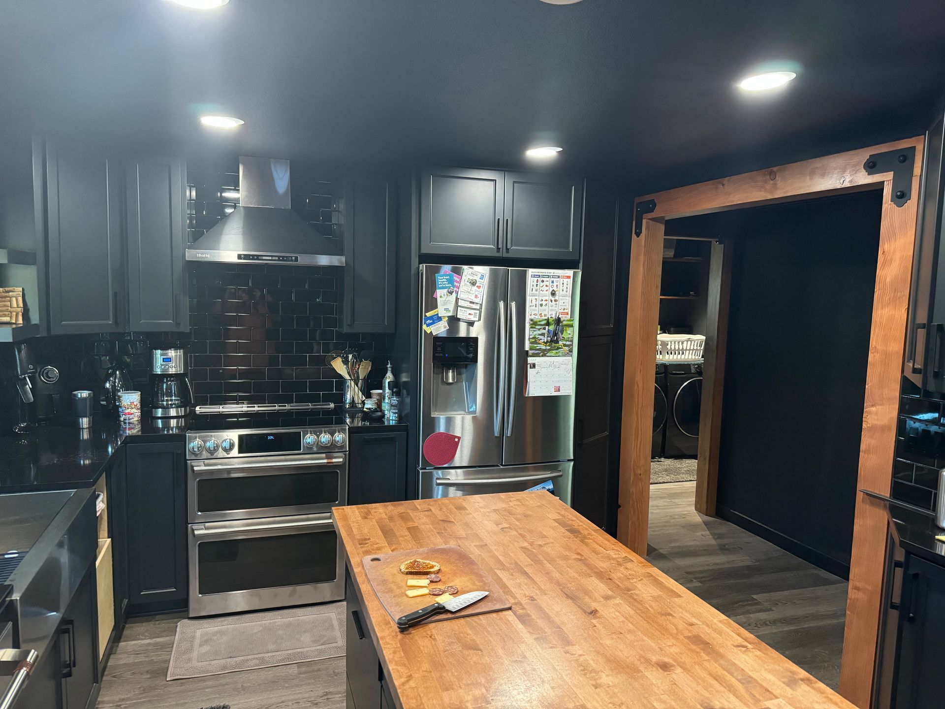 Modern kitchen with dark cabinets, stainless steel appliances, and a wooden island opening into a hallway