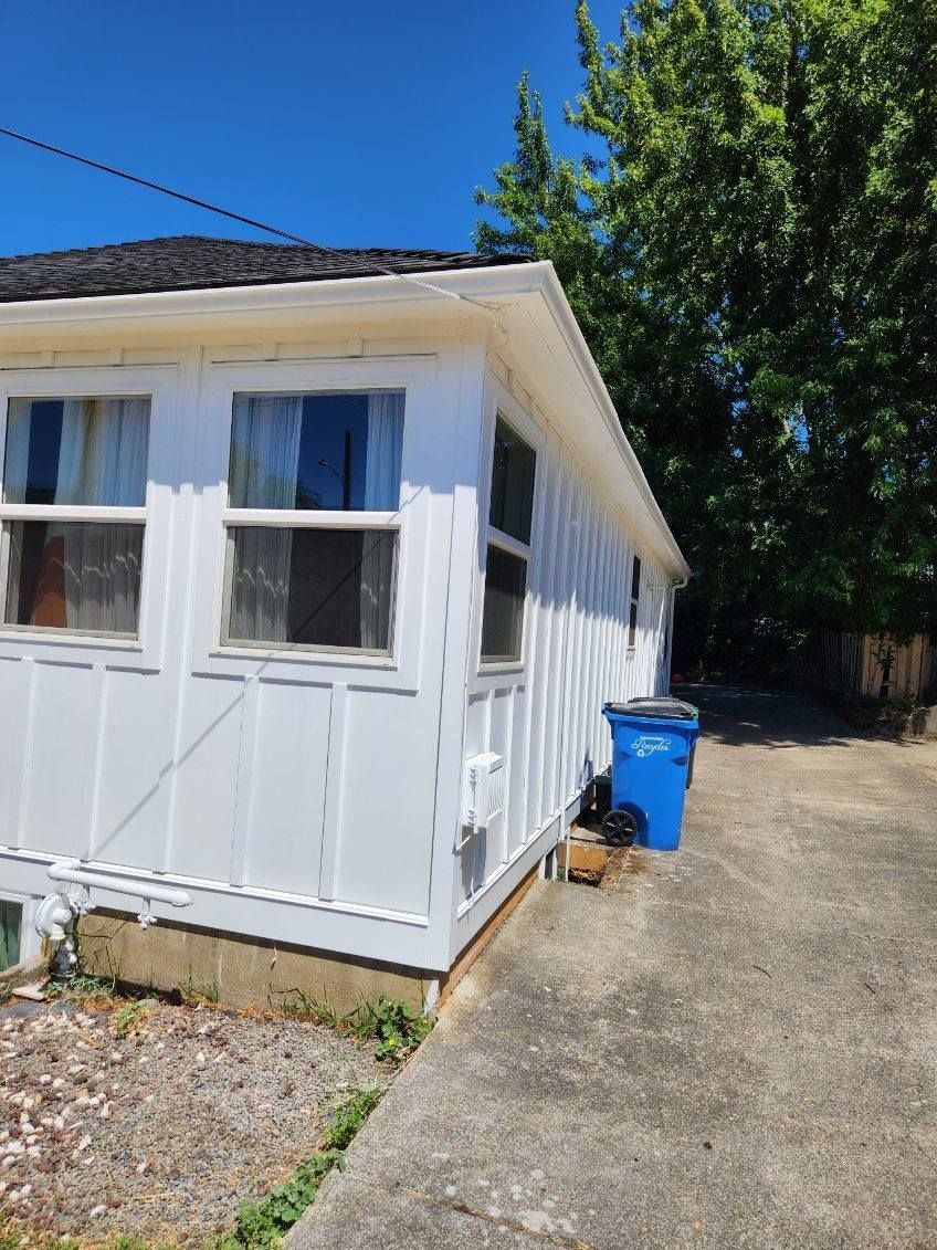 White mobile home with blue bin beside a gravel driveway under a sunny sky