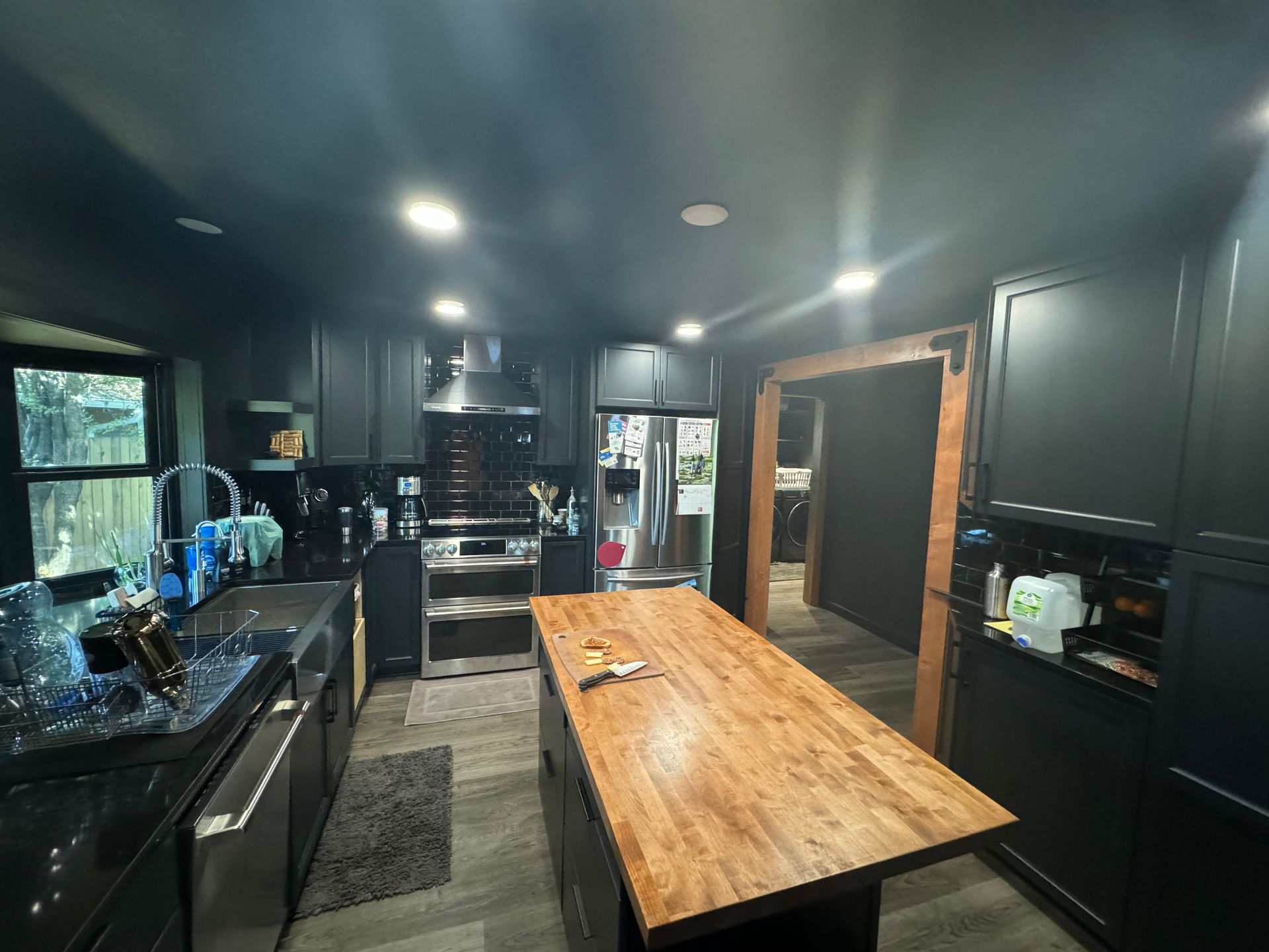 Modern dark kitchen with black cabinets, stainless appliances, and a long wooden island counter