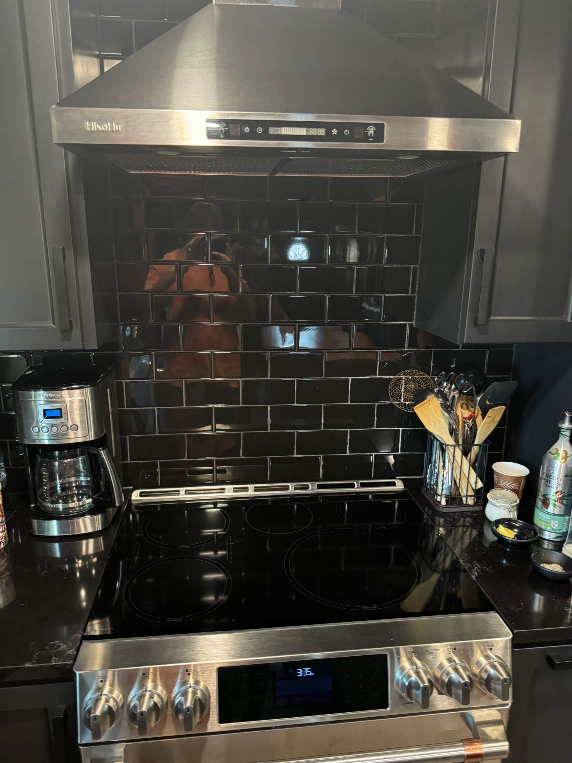 Stainless steel stove with black cooktop and range hood in a kitchen, with a coffee maker and utensils on the counter