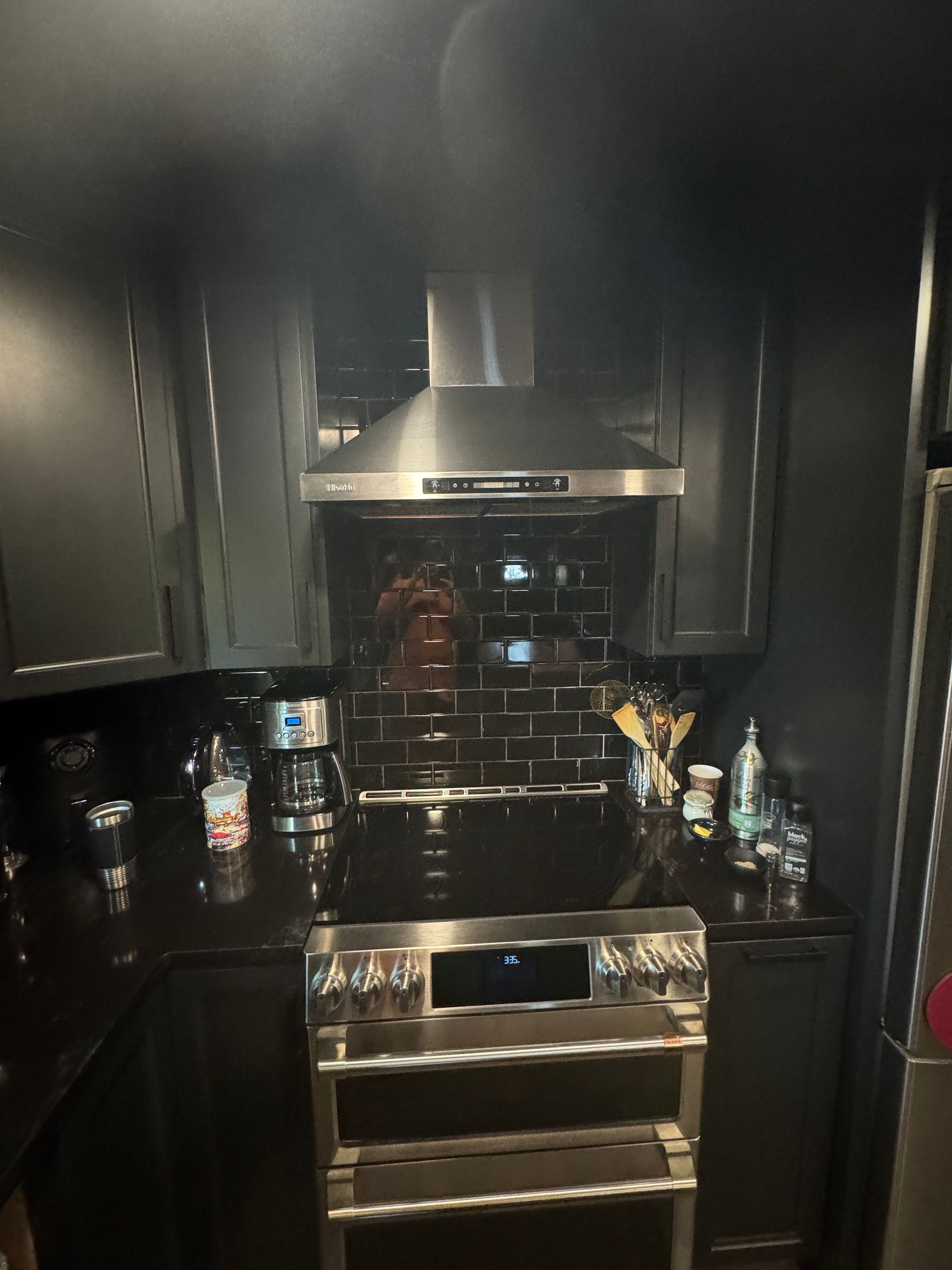 Dark modern kitchen with stainless steel stove, range hood, and countertop items beside it
