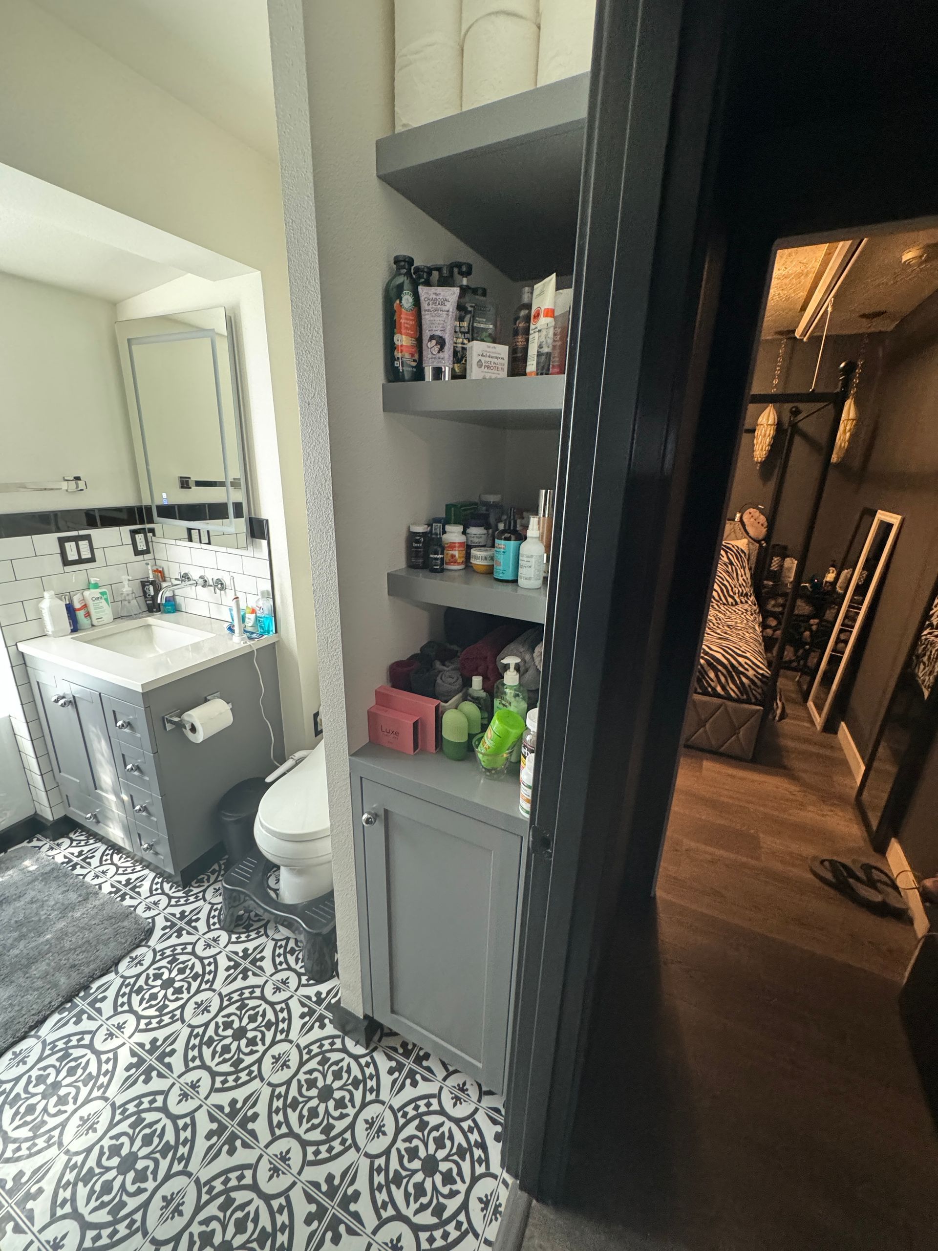 Bathroom with patterned black-and-white tile, sink, toilet, and gray shelving stocked with toiletries.