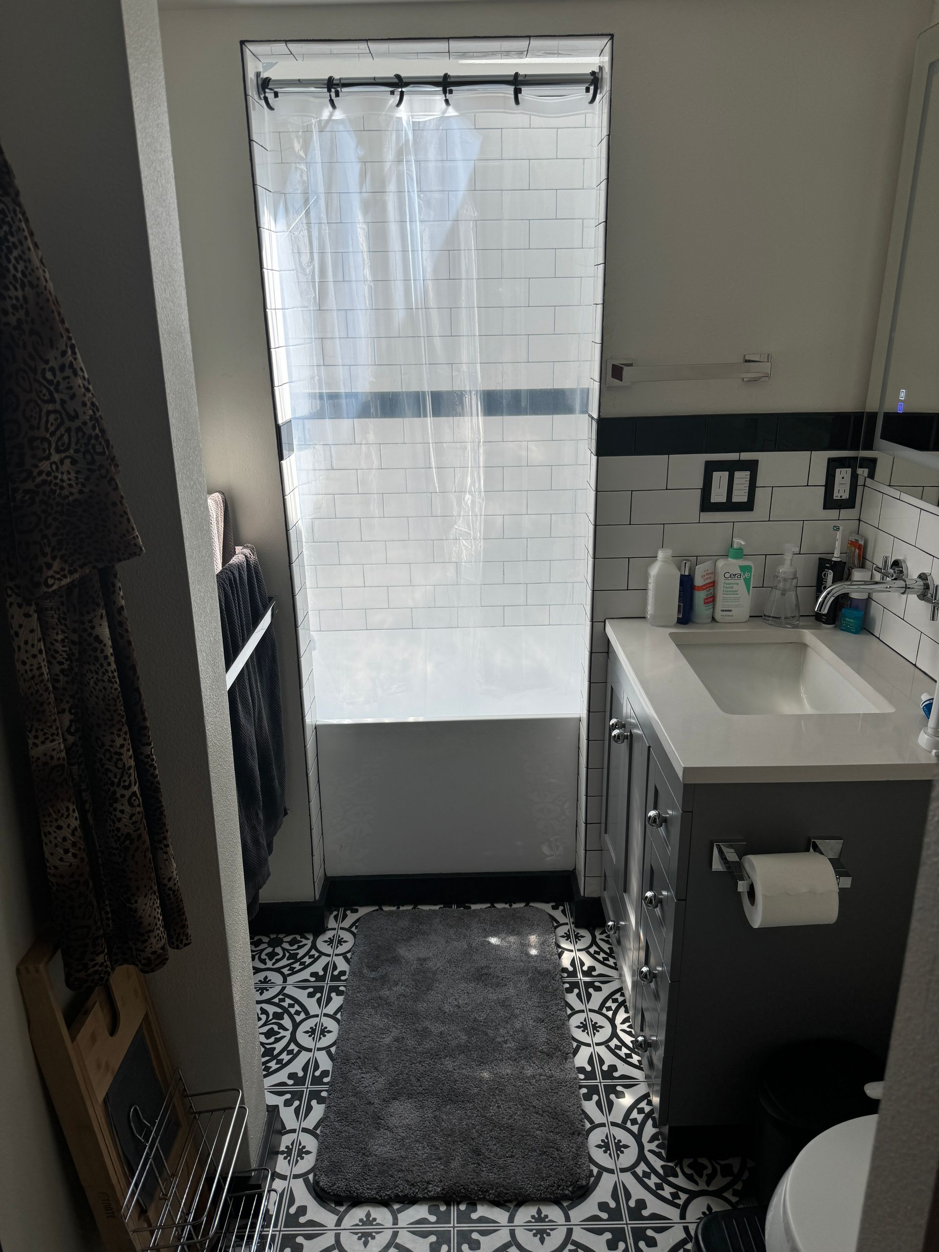 Bathroom with vanity and sink, patterned floor, shower curtain, and frosted window at the end of a narrow room