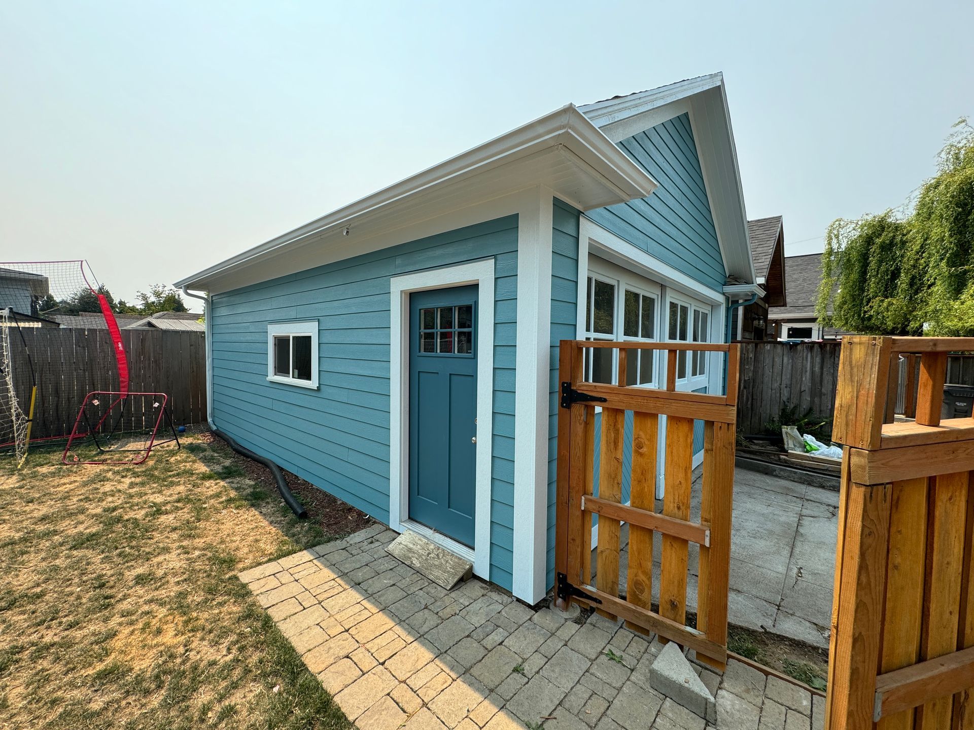 Blue wooden shed with white trim and a small porch gate in a fenced backyard