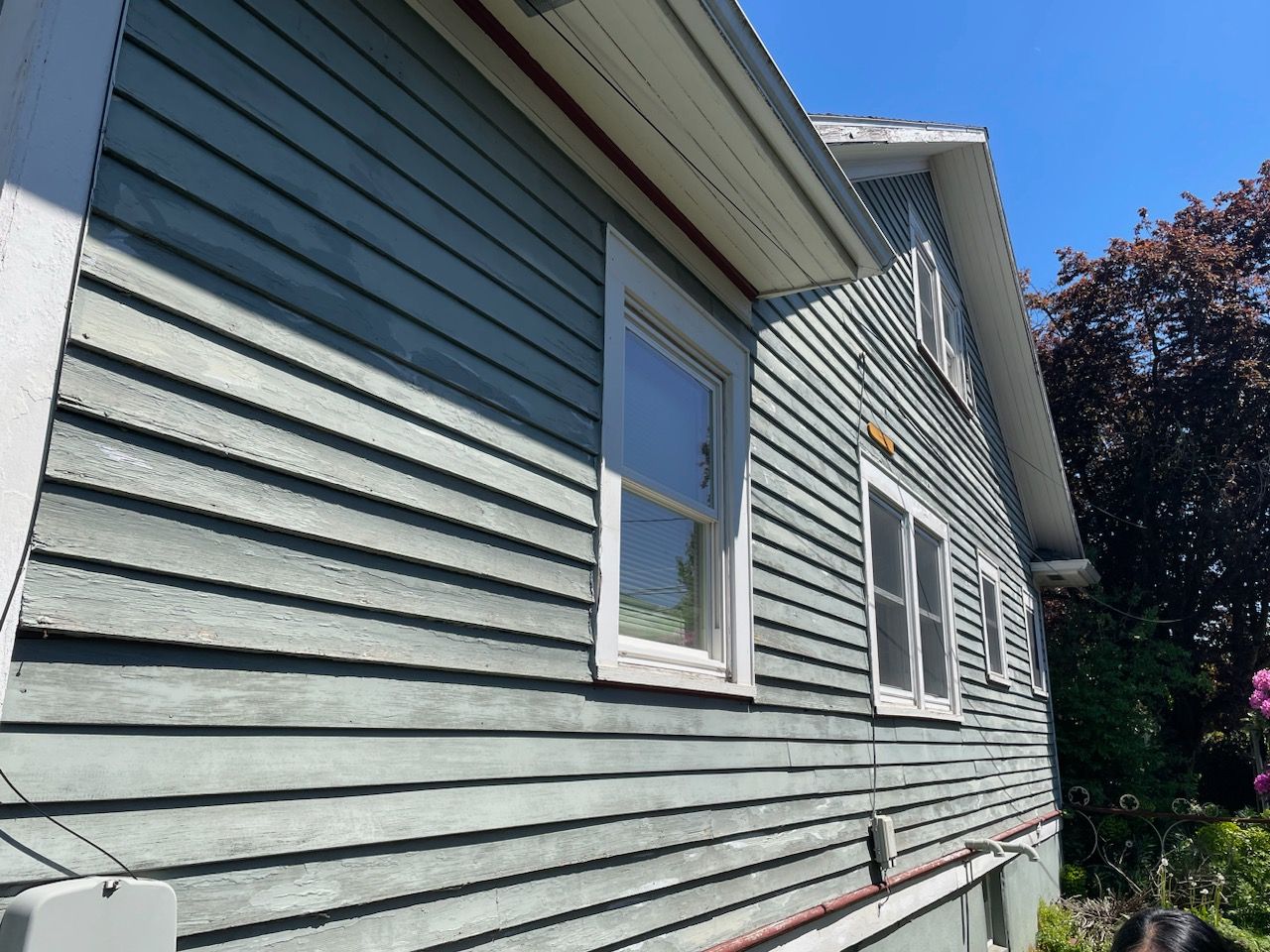 Side view of a gray house with white trim and windows under a blue sky