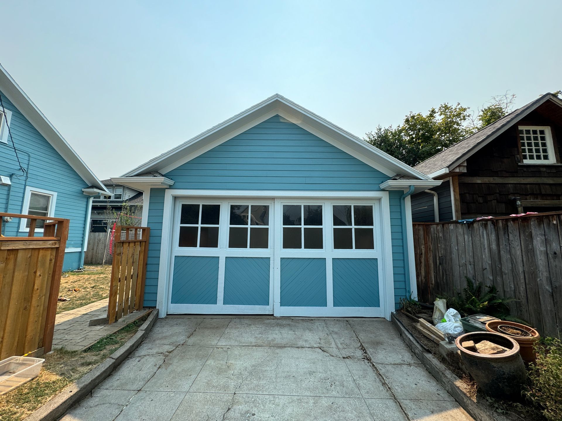 Blue detached garage with double white doors and concrete driveway under a clear sky