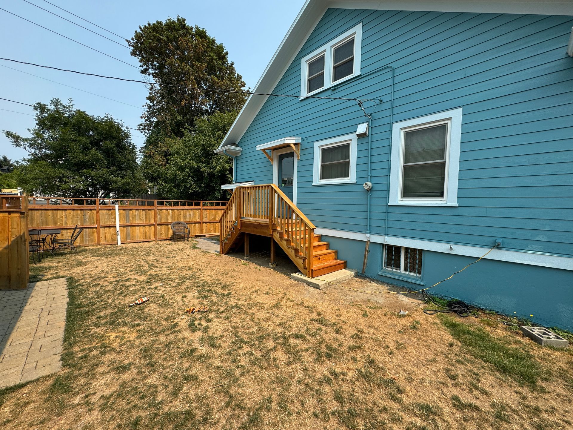 Blue house with wooden ramp and fenced yard on a dry lawn.