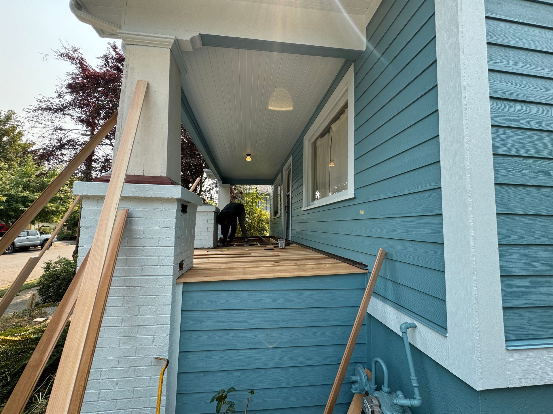 Blue house porch with steps, wooden ramp, and two people standing inside the entryway