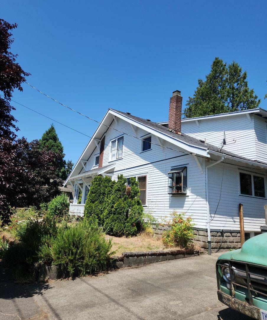 White house with porch and chimney beside a driveway under a clear blue sky
