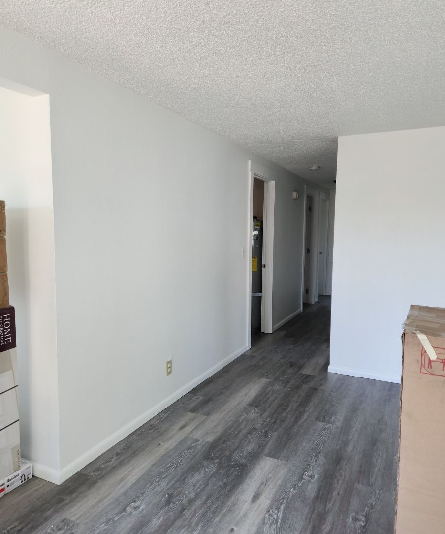 Empty hallway with gray wood flooring, white walls, and doors leading into rooms.