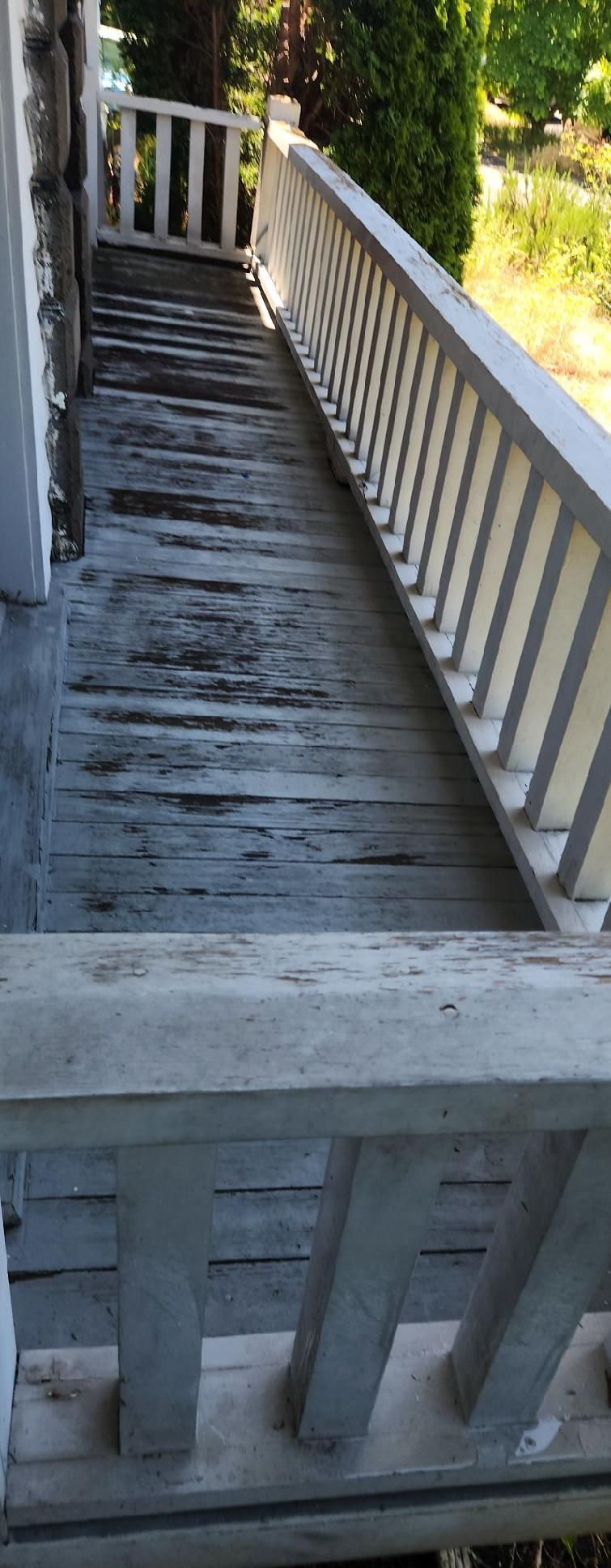 Weathered wooden deck staircase with white railings in a sunny outdoor setting