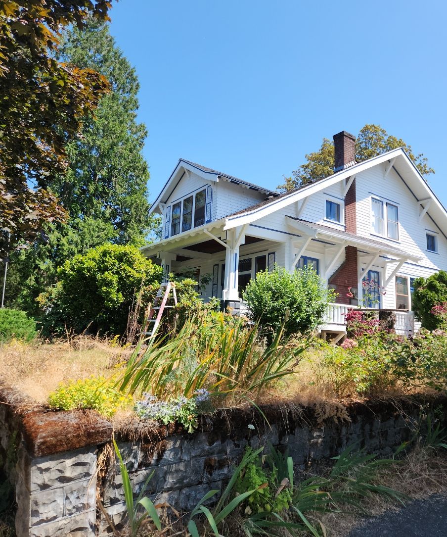 White house with a front porch on a grassy hillside under a clear blue sky.