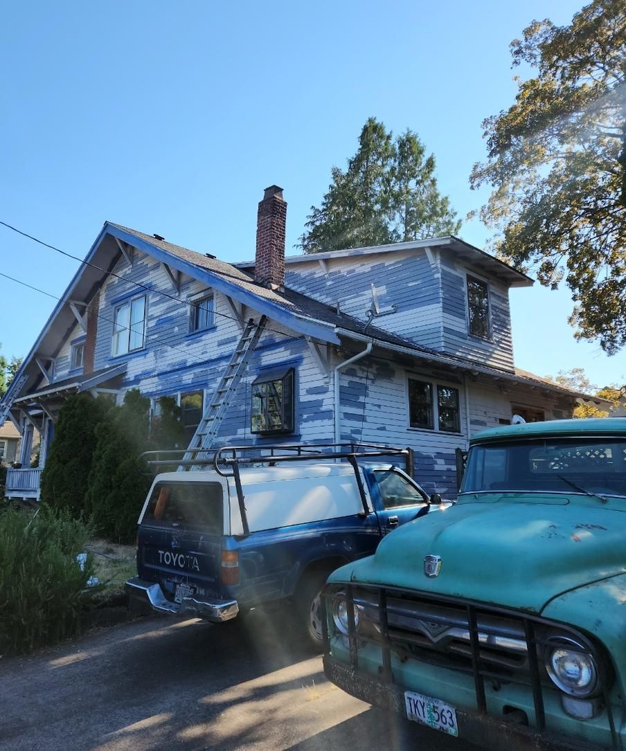 Two old vehicles parked beside a weathered blue house with peeling paint