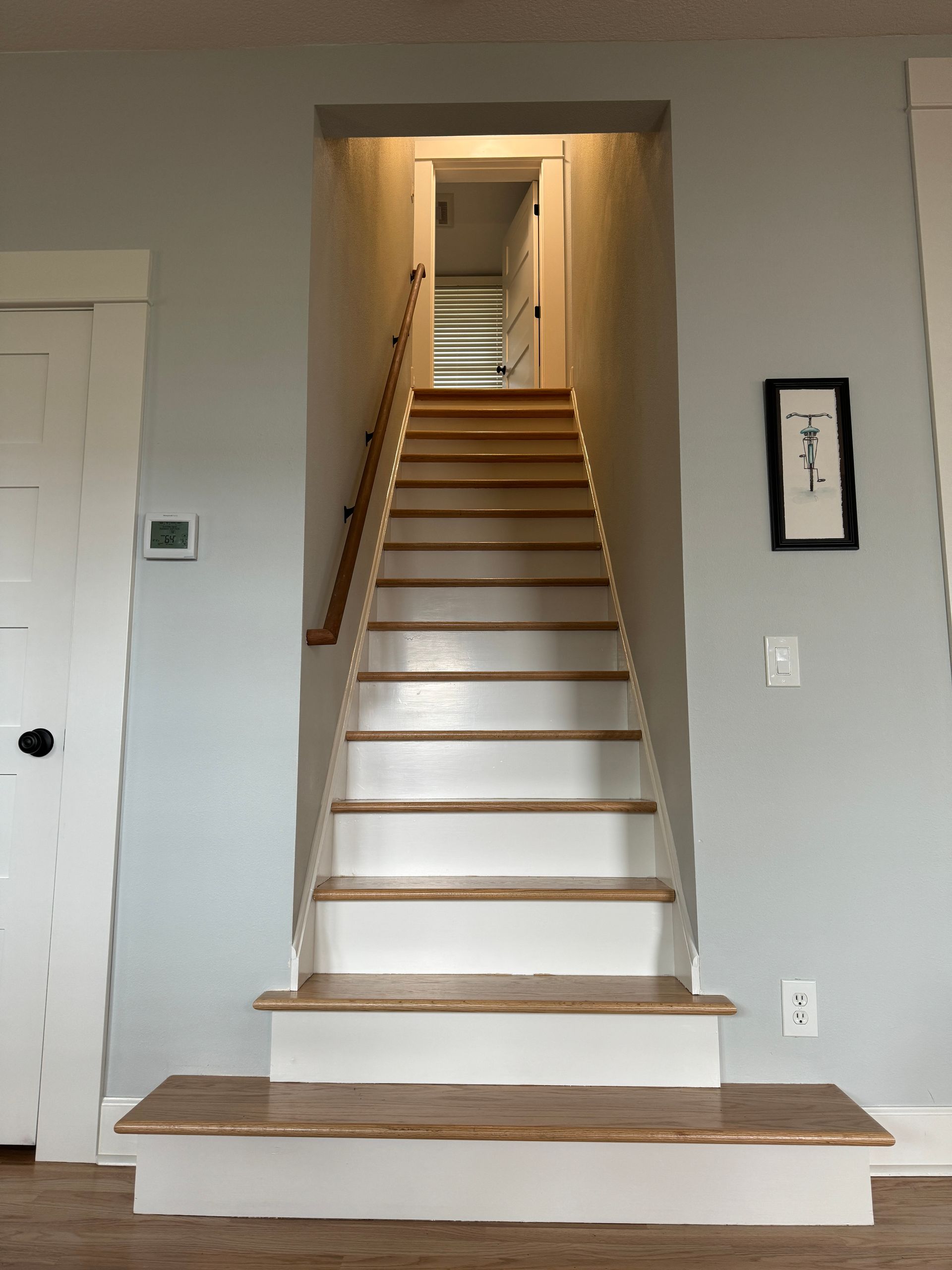 Steep indoor staircase with white steps and wood trim in a gray-walled hallway.