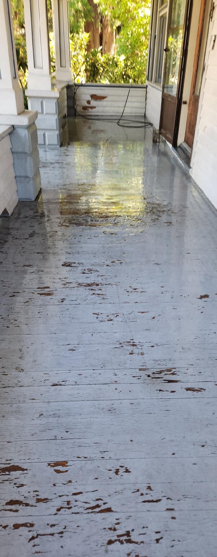 Narrow porch with wet concrete floor, white walls, and sunlight reflecting from the end.