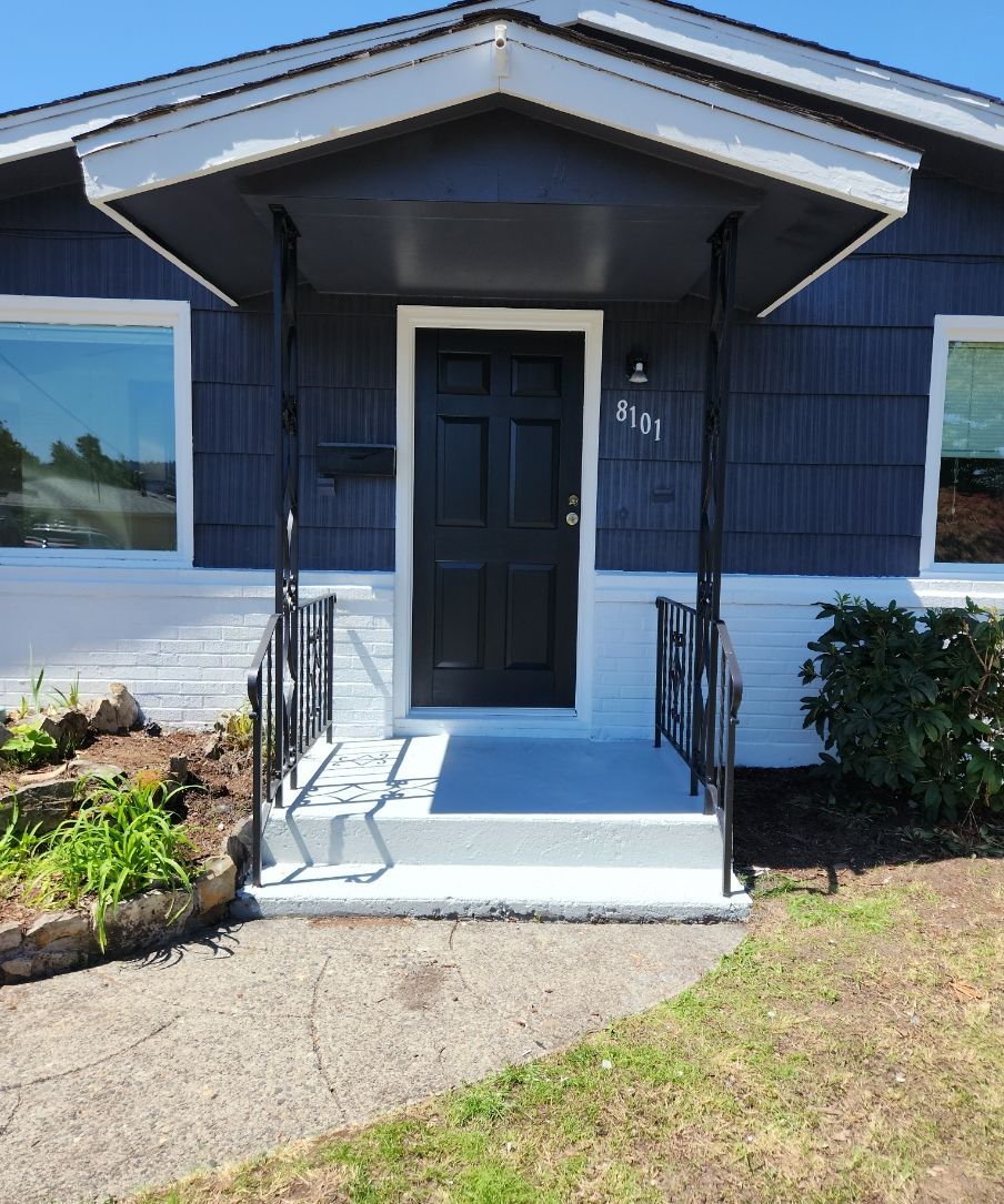 Front entrance of a blue house with a black door, small porch, steps, and garden path.
