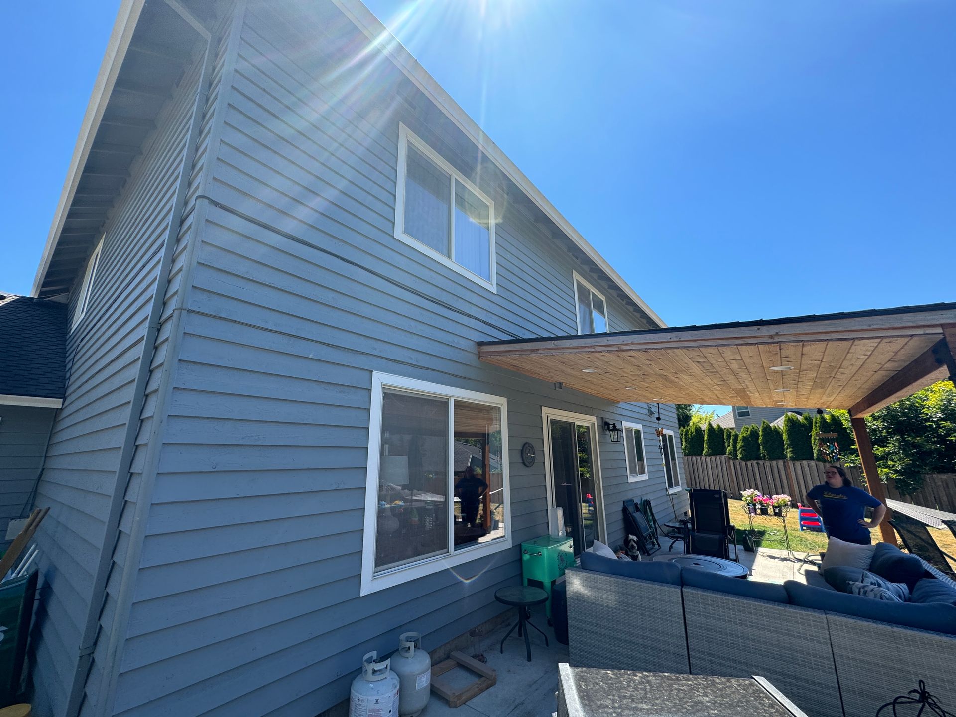 Blue-gray house exterior with covered patio, gray sofa, and people gathered in the backyard