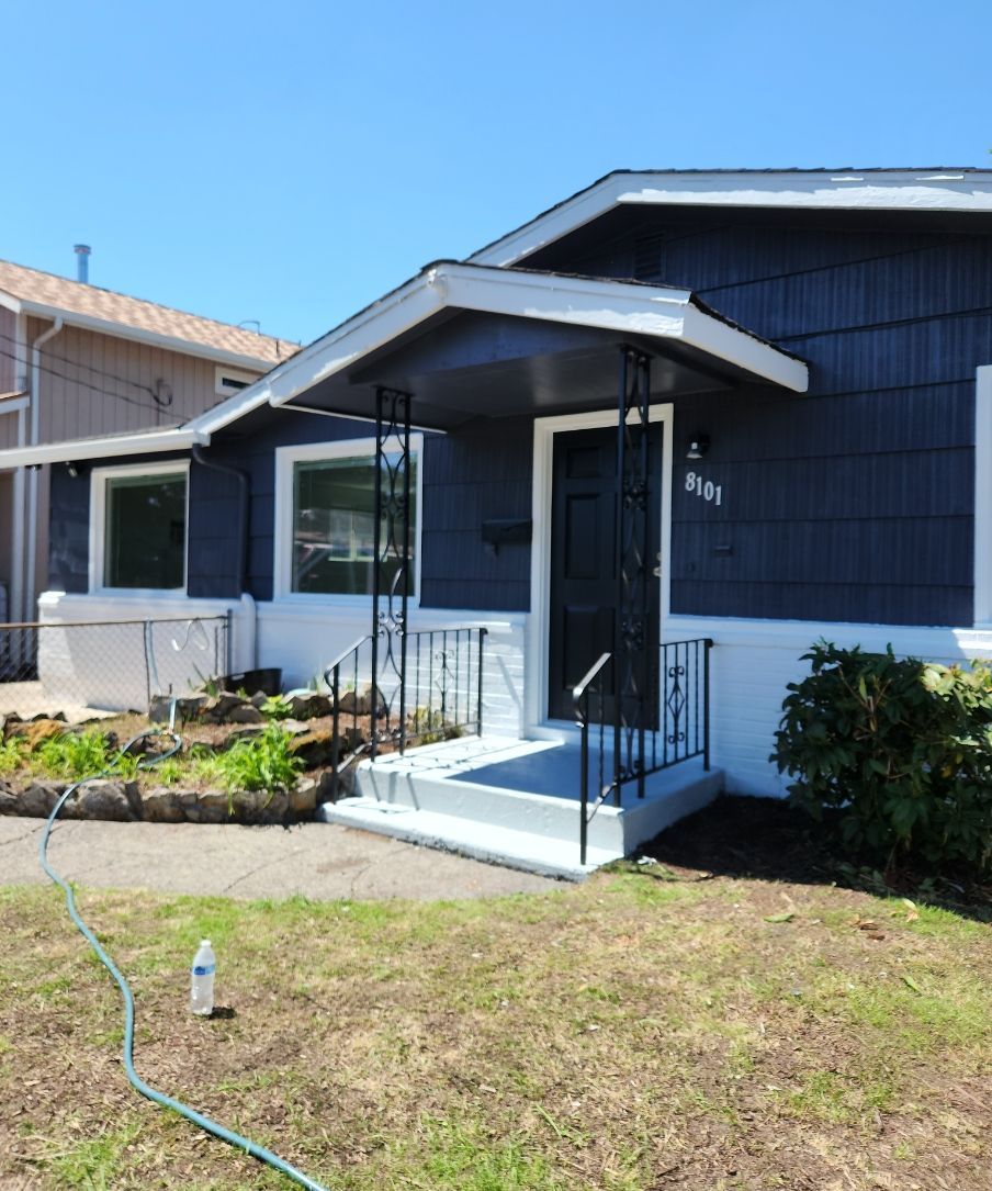 Small dark-blue house with a front porch, steps, and a grassy yard under a clear sky.