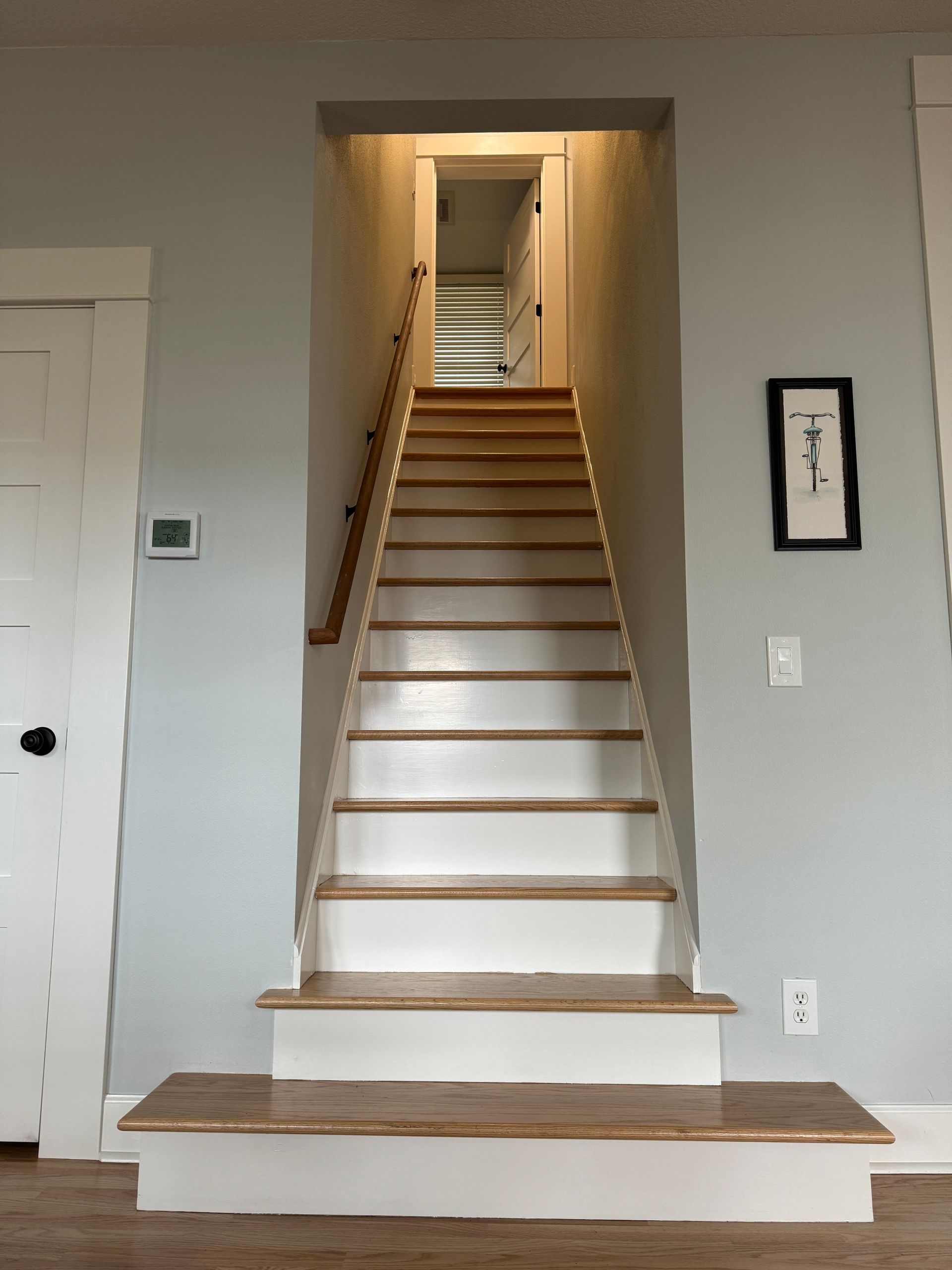 Indoor staircase with white steps and wood trim leading to an upper hallway through a doorway
