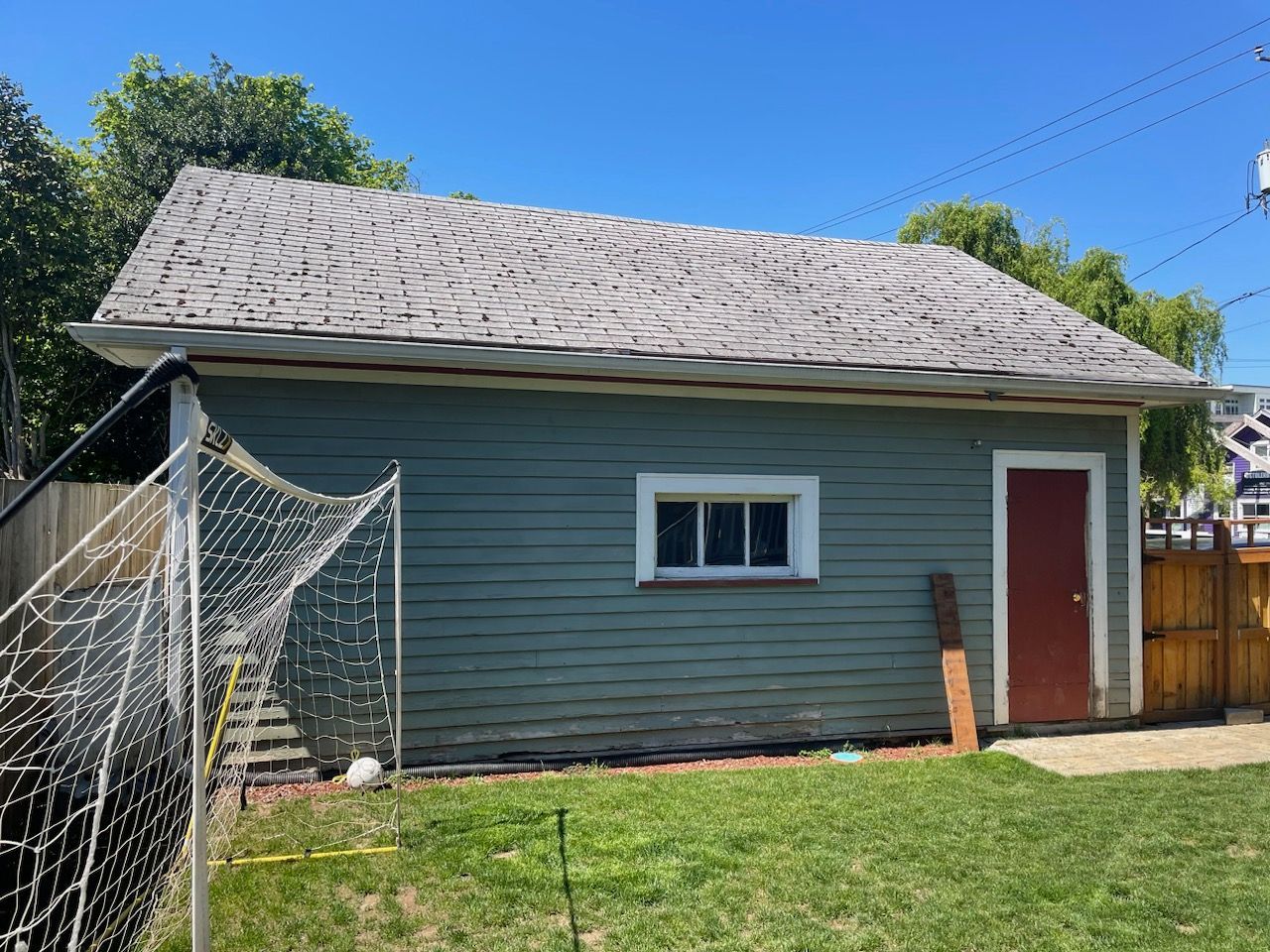 Small gray shed with a red door and chain-link fence in a sunny yard