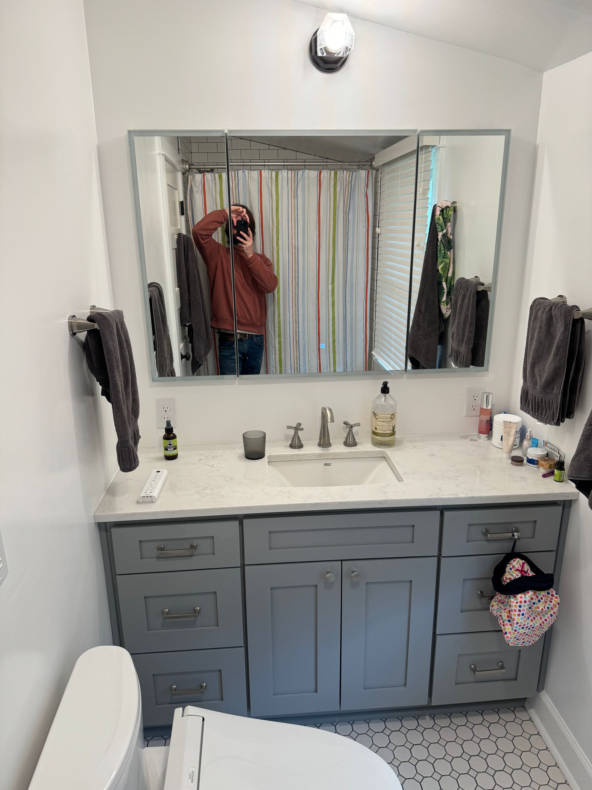 Bathroom vanity with gray cabinets, white countertop, large mirror, and a wall light above it.