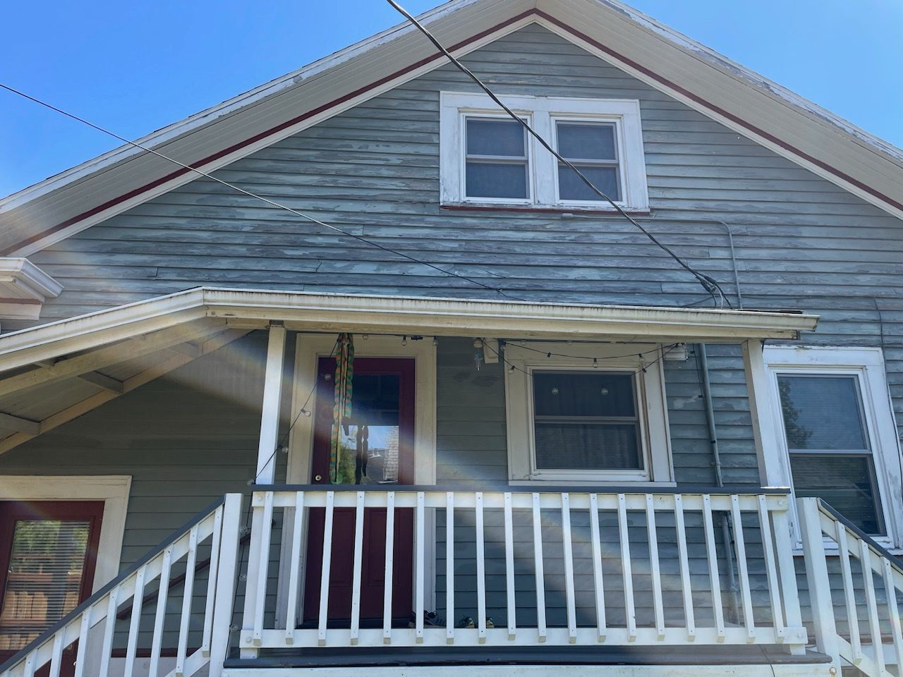 Weathered gray house with a front porch, white railing, and red door under a gabled roof.