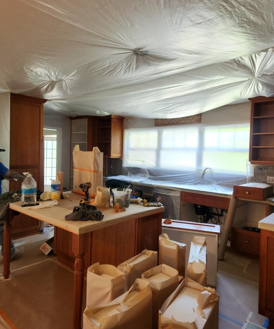 Kitchen under renovation with plastic-covered ceiling, unpacked boxes, and cluttered island counters.