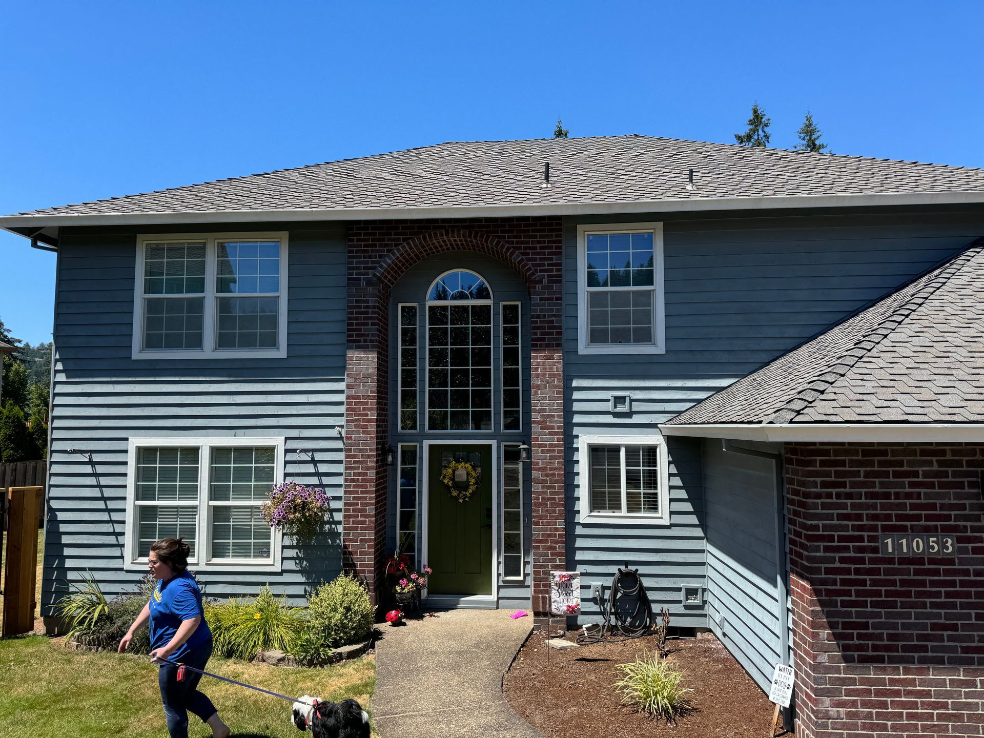 Two-story blue house with brick accents and a front entrance, with a person walking on the lawn
