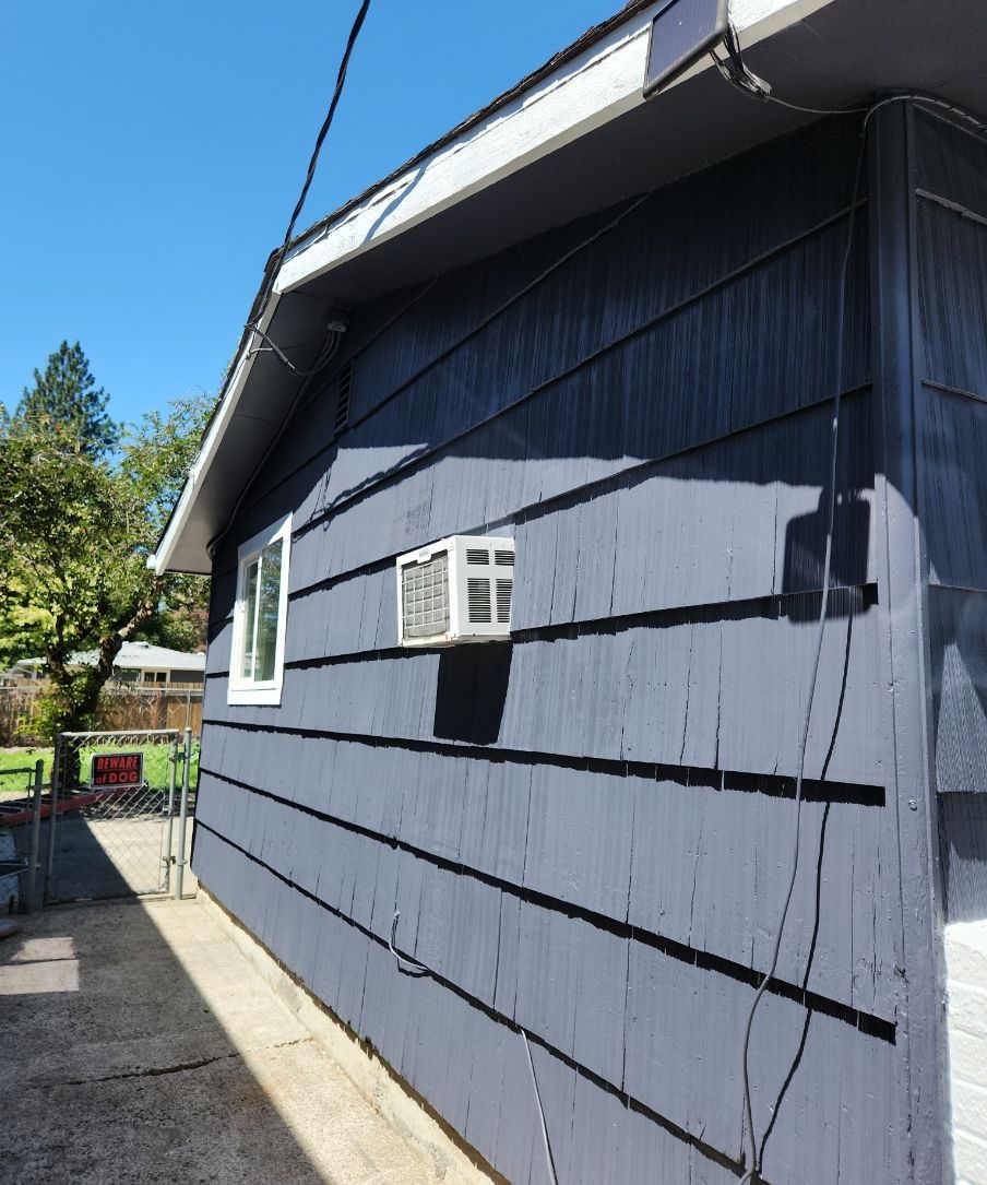 Blue-gray house exterior with white-trimmed window and narrow concrete walkway beside a fence.