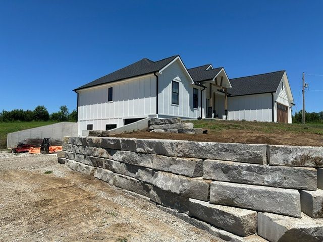 A large white house is sitting on top of a hill next to a stone wall
