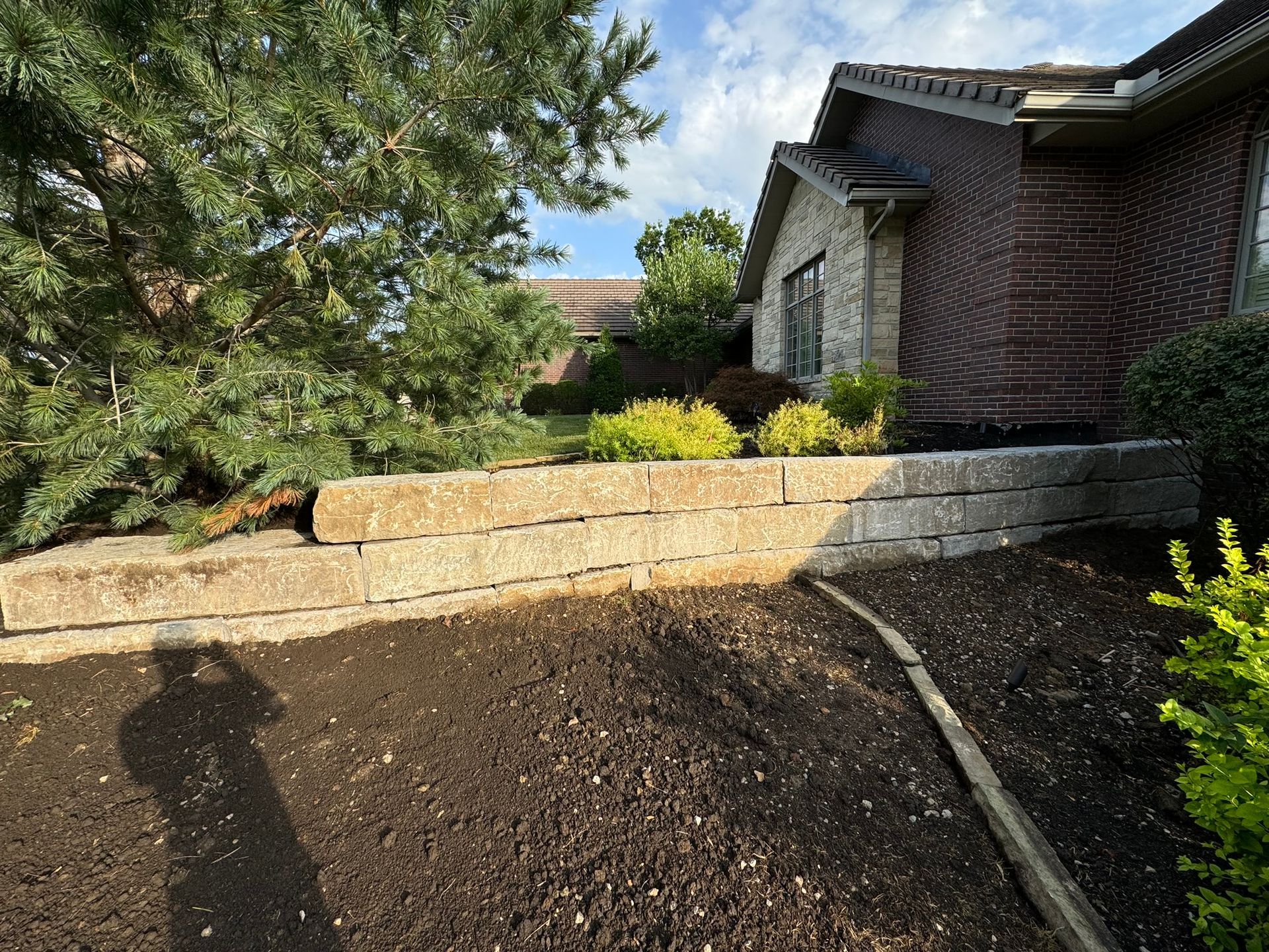A brick wall in front of a house with a tree in the background.
