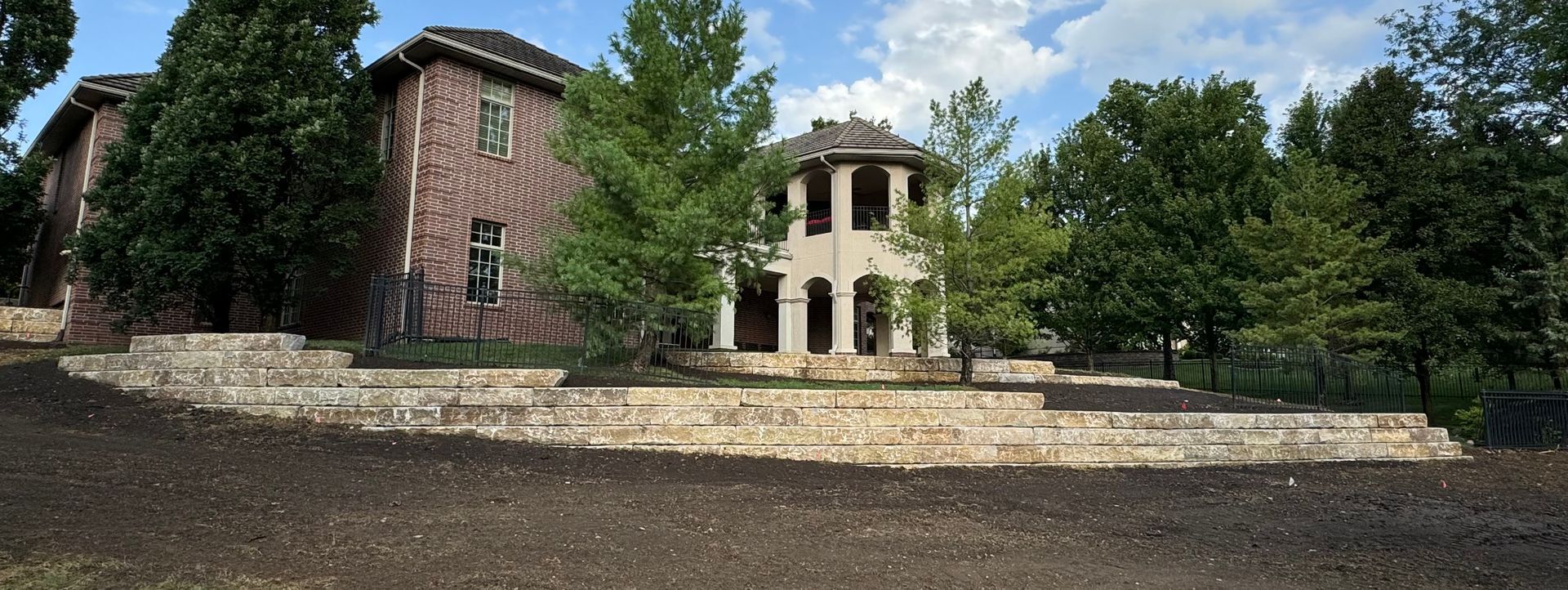 A large house is surrounded by trees and a stone wall.