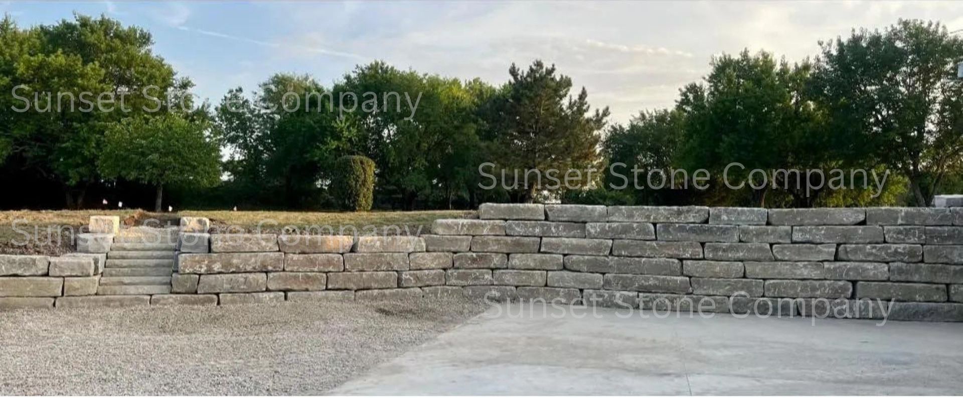 A large stone wall is surrounded by trees and gravel