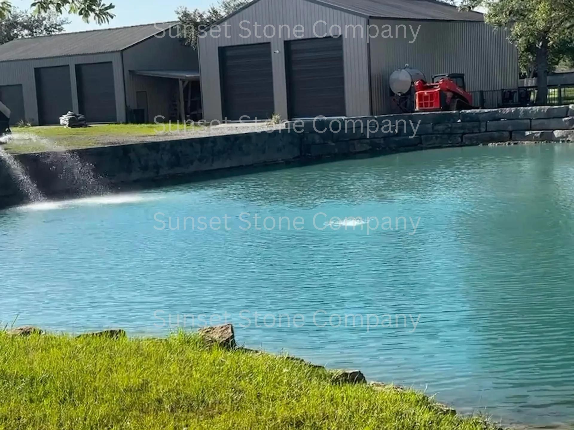 A pond with a fountain in front of a building that says sunset stone company