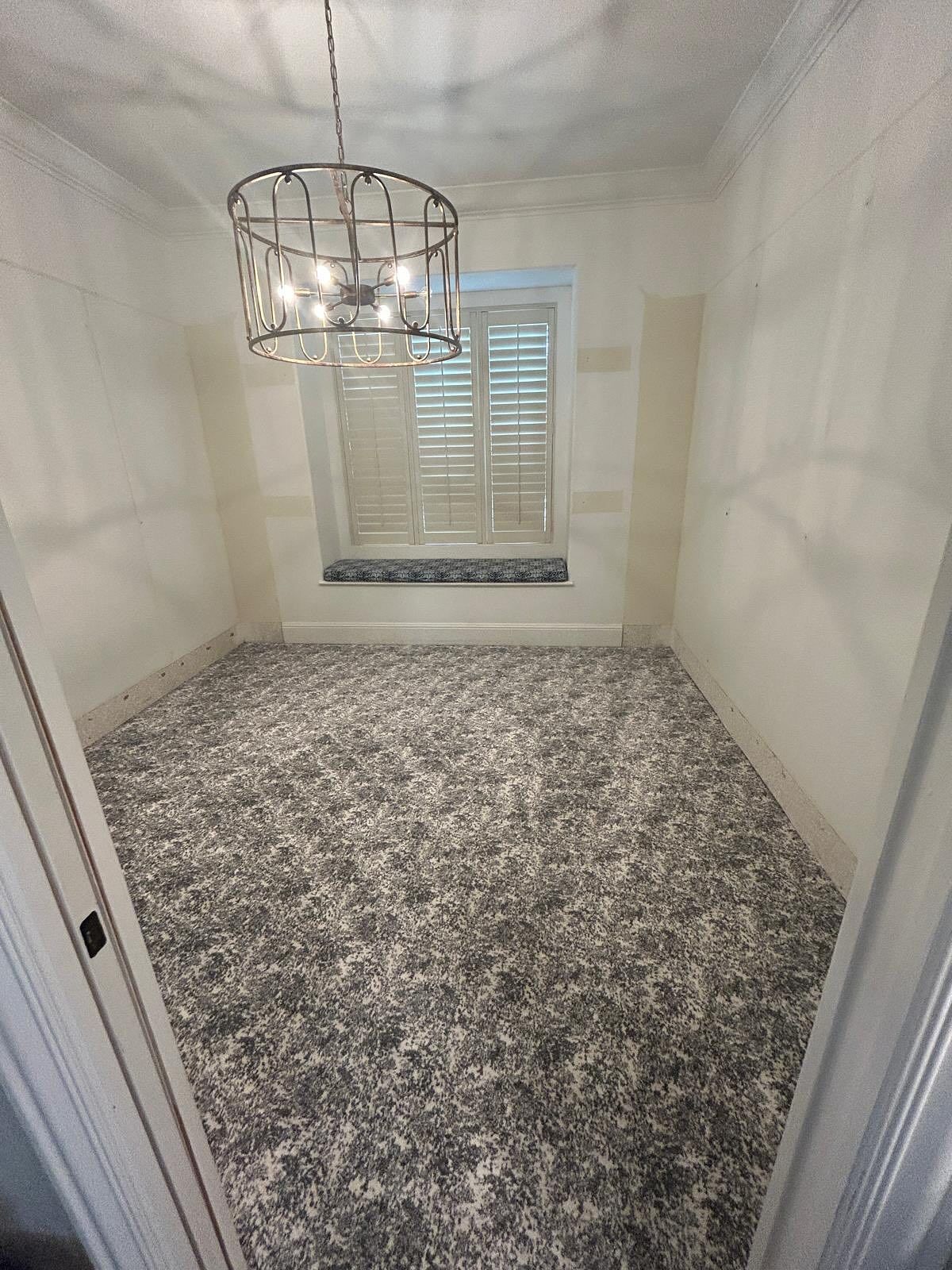 Small room with patterned carpet, window with shutters, and chandelier.